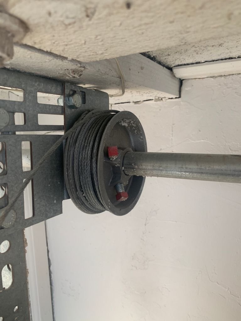 A garage door cable on a wheel. It has a red ring. The track is metal.