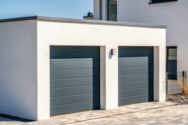 Two modern sectional garage doors on a white building with a paved driveway.